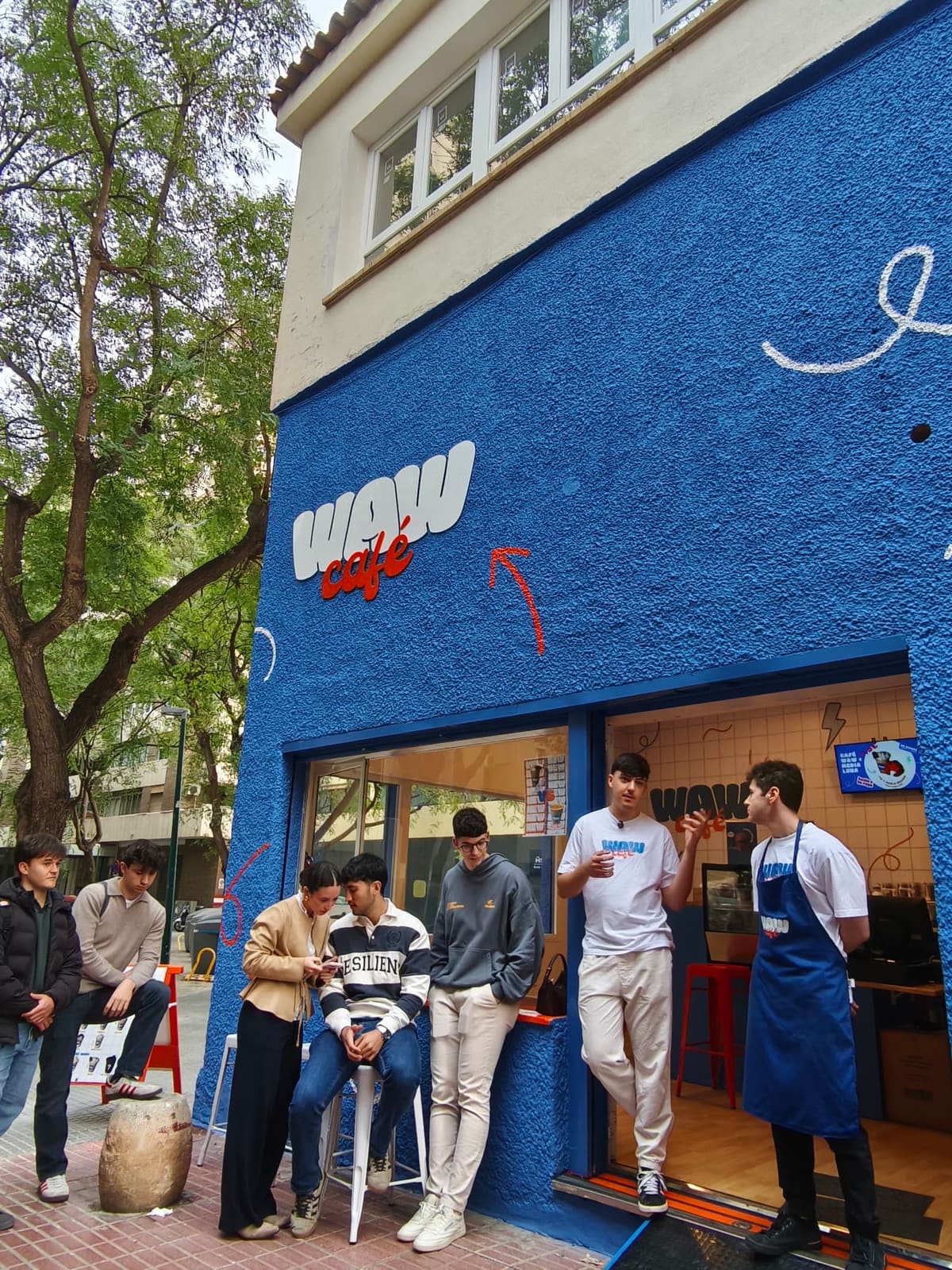 Fachada azul de WAW Café con asistentes al networking en la puerta